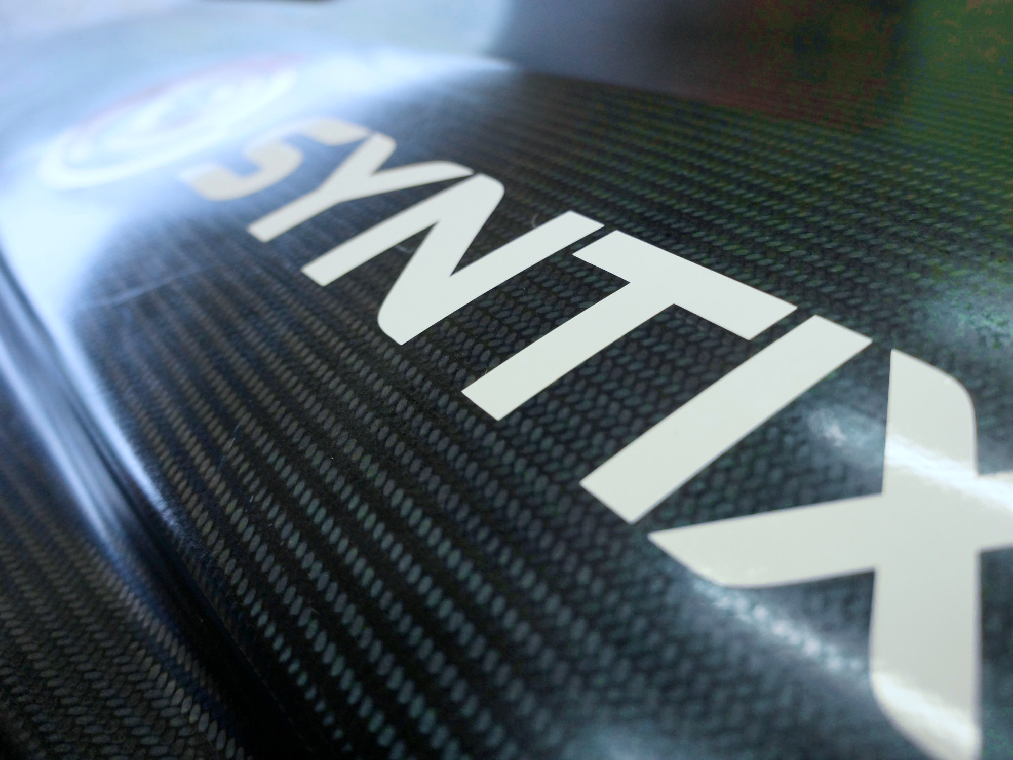 Close-up of the Syntix wordmark in white on a dark carbon fiber surface