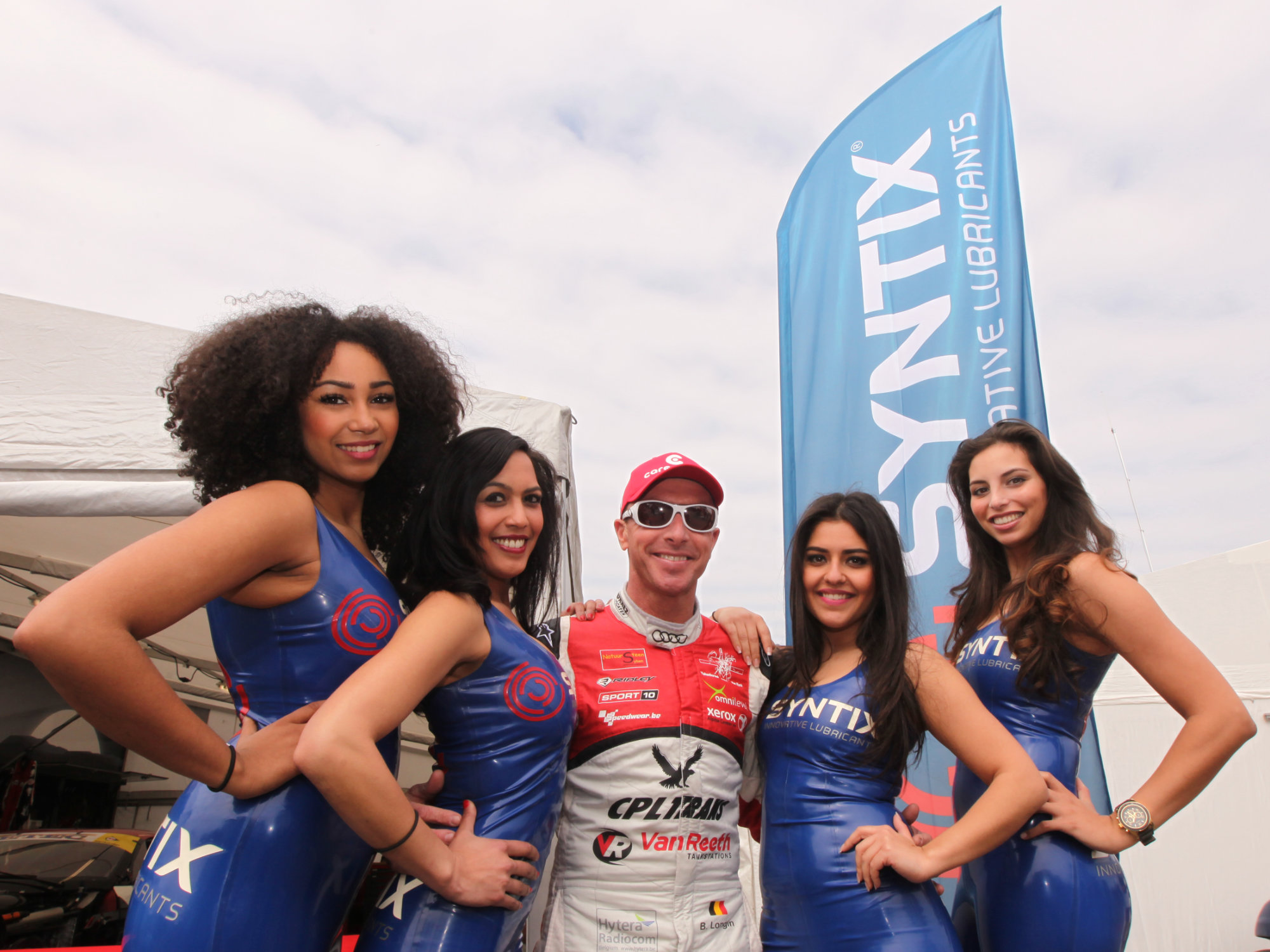 Promotional grid girls in Syntix-branded latex outfits at a motorsport event, displaying brand colors and logo