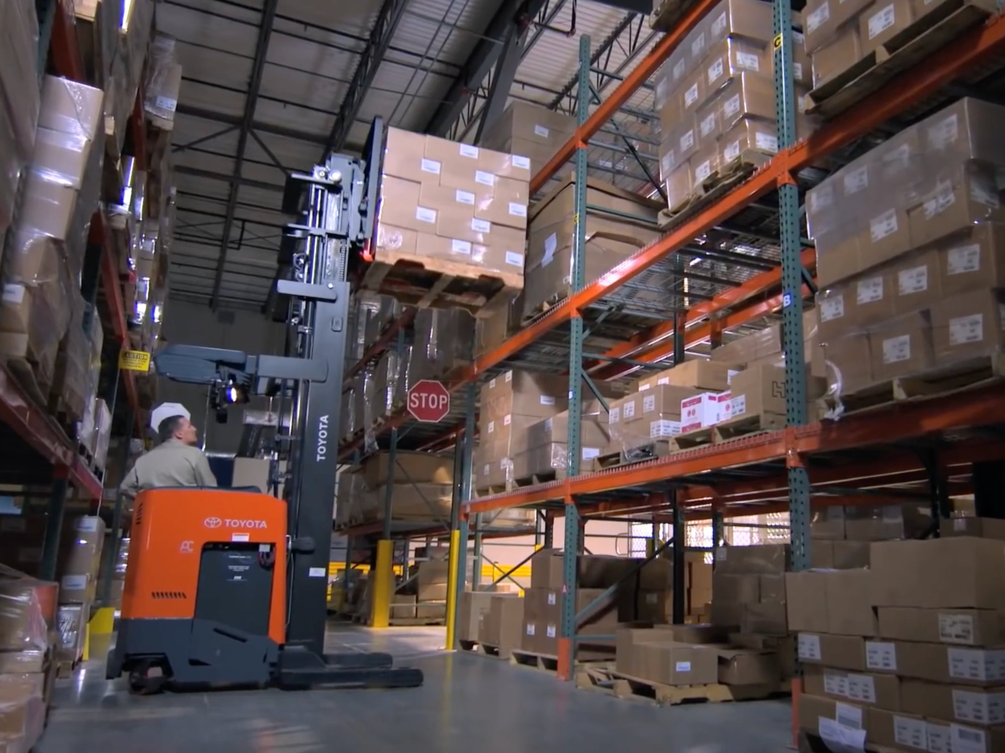 Toyota forklift lifting pallet in a high-rack warehouse environment